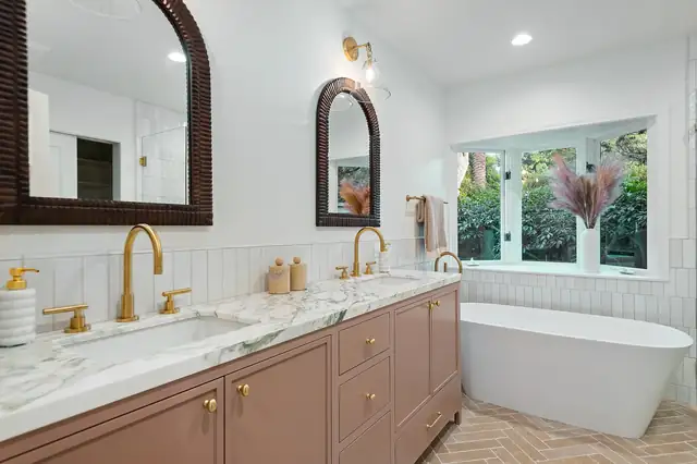 Primary bathroom remodel with a double vanity, marble top, brass faucets, freestanding tub and herringbone floor