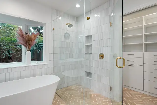 Primary bathroom with a freestanding tub, a glass shower with stacked white tile and brass fixtures