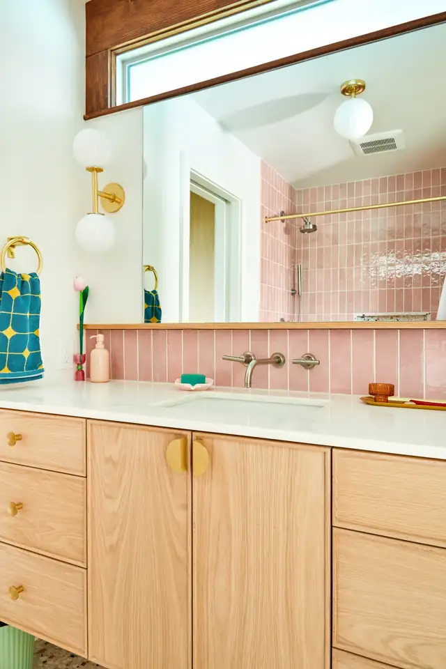 Guest bathroom remodel with pink tile, a white oak vanity and brass wall-mounted faucet