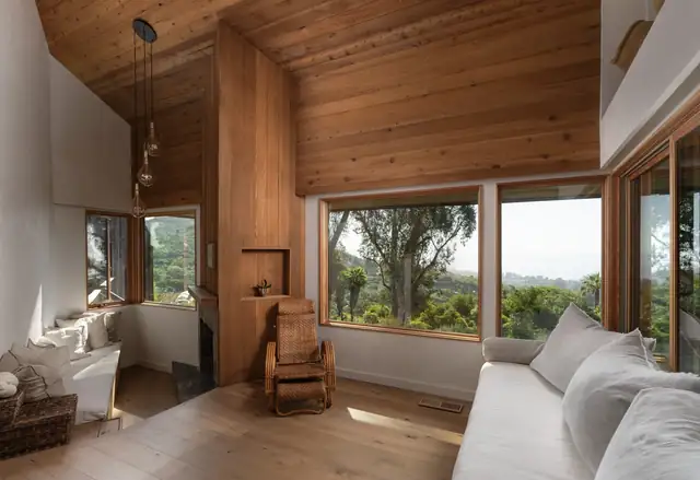 Remodeled living room with a wood plank ceiling and large windows facing the trees