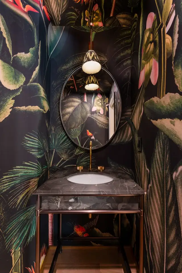 Montecito powder room with dark tropical wallpaper, an oval mirror and a stone vanity on a metal stand